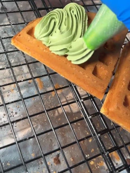 Matcha cream being piped onto a fresh waffle on the cooling rack.